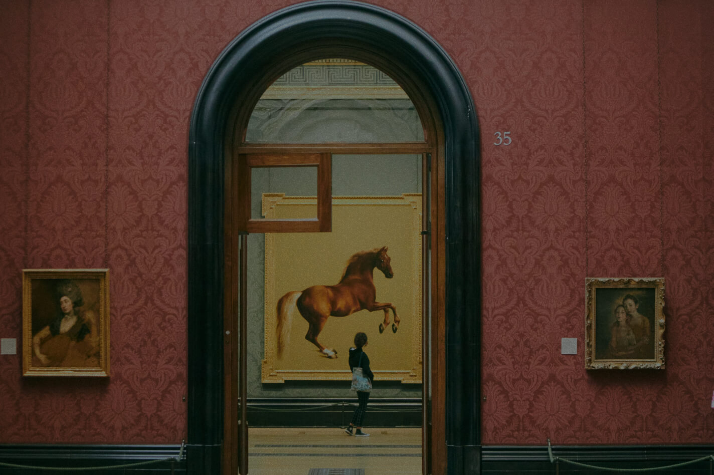 A girl looking at a painting of a horse at the National Gallery in Trafalgar Square, London.